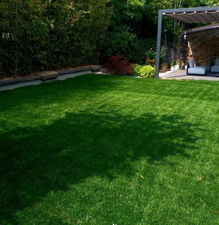 Well-manicured green lawn in a modern backyard with pergola, dense hedges, and stone structures visible in background